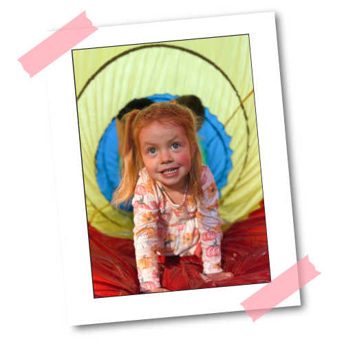 A toddler crawling through a rainbow tunnel at open gym